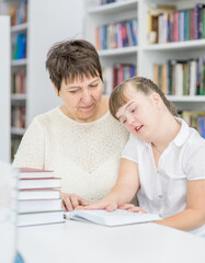 Wall Mural - Senior woman helps to girl with syndrome doing homework at a school. Education for disabled children concept