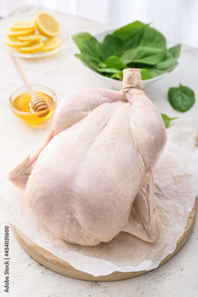 Board with whole raw chicken on light background, closeup