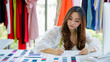 © Bangkok Click Studio - Cute and enerfyful female Asian designer working at desk in design room among clothes and fabric color sample