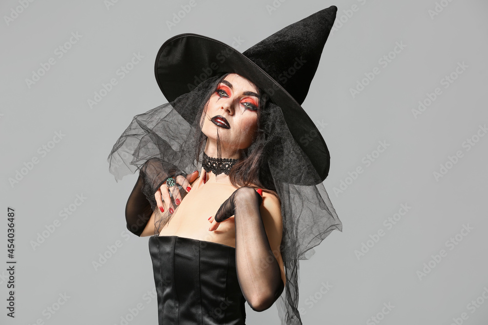 Beautiful woman dressed as witch for Halloween on grey background