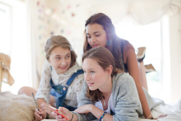 Canvas Print - Three teenage girls using smart phone together while lying on bed in bedroom