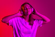 © Lustre Art Group  - Beautiful young caucasian girl with with closed eyes listening to music in headphones isolated on pink background in neon