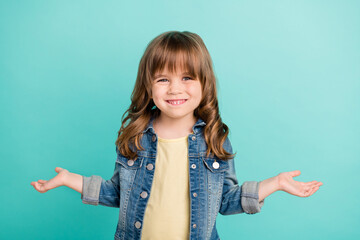 Photo of positive small girl shrug shoulders look camera wear jeans jacket isolated aquamarine color background