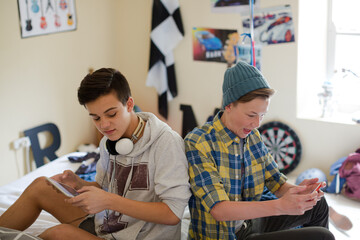 Two teenage boys using electronic devices in room