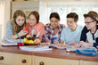© KOTO - Group of smiling teenagers gathered around table in dining room