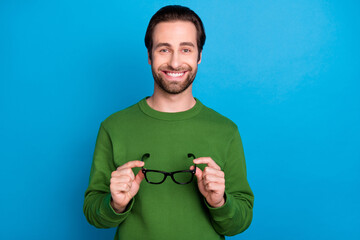 Sticker - Photo of young good mood handsome smiling businessman hold glasses wear green sweater isolated on blue color background