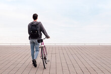 Rear View Of Young Man Walking Pushing A Bicycle