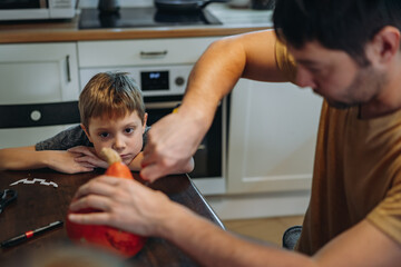 Caucasian man with his cute 6 year old son drawing out eyes on a pumpkin to make traditional Jack lantern.