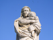 Mary Of God With The Little Jesus Christ In Her Arms. Stone Monument In The Cemetery