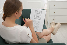 Young Woman Solving Sudoku Puzzle On Sofa Indoors