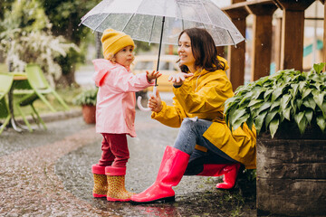 Mother with daughter walking in park in the rain wearing rubber boots