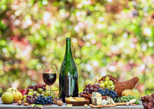 Grapes, Bottle Of Wine And Different Cheeses On Country Wooden Table And Blurred Colorful Autumn Background. Variety Of Products As The Symbol Of Autumn Abundance And Prosperity.
