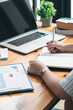© NAMPIX - Cropped shot of woman hand writing on notebook with pen while sitting at the table with laptop and business graph, vertical view.