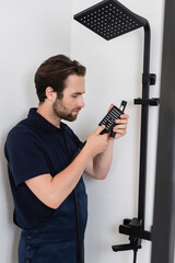 Wall Mural - young plumber in uniform checking shower head in modern bathroom