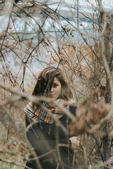 Poster - Vertical shot of a Caucasian female through branches of a tree dressed in a black dress and a scarf