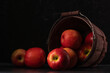 Dark and moody view of apples spilling from a bucket on dark color table and background
