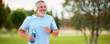 Happy Mature Man Wearing Headphones With Water Bottle In Hand Jogging Outside In City Park