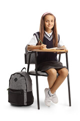 Poster - Girl in a school uniform sitting in a school chair with a pen and a notebook and looking at camera