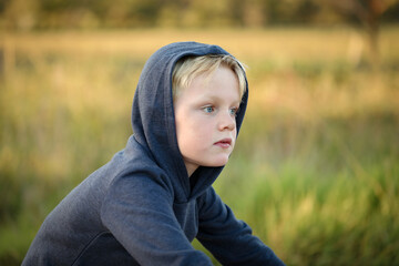 Wall Mural - Young blonde boy wearing hoodie riding bike on dry country lane