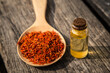 Safflower in wooden spoon and a bottle of essential oil on old wooden plate.
