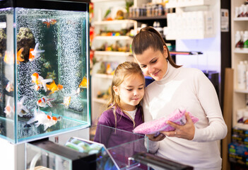 Wall Mural - Happy young mother with cute little daughter choosing accessories for home aquarium in pet shop