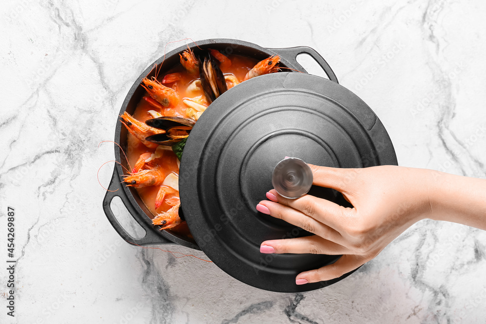 Female hand with pot of tasty Cacciucco soup on light background