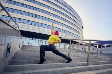 Wall Mural - sporty woman in bright sports clothes and dyed pink hair stretches against background of building