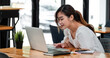 © Natee Meepian - Smiling asian girl student using laptop computer study online with teacher, happy young woman learn language listen lecture watch webinar write notes look at laptop sit in cafe, distant education.