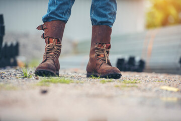 Wall Mural - Men wear construction Boots safety footwear for worker at construction site. Engineer Wear Jeans Brown Boots Worker on Background of Refinery. Engineer safety industry fashion footwear walking outdoor