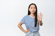Asian woman say no. Teen girl extend one hand, taboo refusing gesture, stop sign, frowning and looking serious at camera, white background