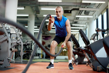 Mature Athlete Exercises With Battle Ropes On Sports Training In Gym.