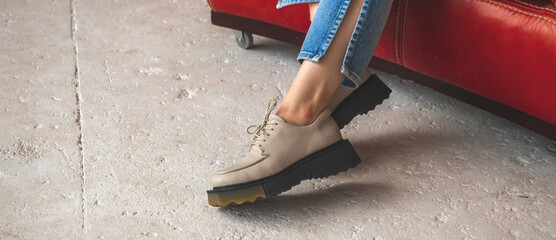 Wall Mural - Urban footwear banner. Casual sneakers on teen girl legs in denim jeans. Teenage sitting on red old leather chair, concrete background photo