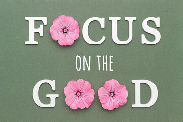 Wall Mural - Focus on the good. Motivational quote from white letters and pink flowers on green background. Creative concept inspirational quote of the day