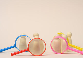 wooden figures of men stand on a beige background and a plastic magnifying glass. Recruitment concept, search for talented and capable employees