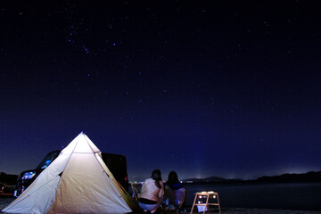 キャンプの夜にテントの隣で星を見上げる2人