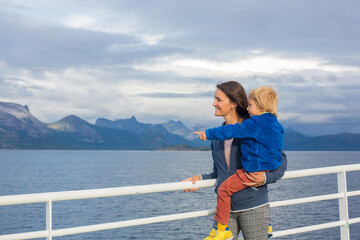 Child and mom, cute blond boy with mother, looking at the mountains from a ferry in Nortern Norway on his way