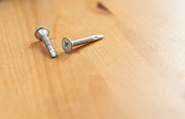 Self tapping sheet metal screws on wood surface.  Close up detail of 2 stainless steel screws on light wood table, room for copy on lower right.