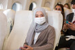 Asian Muslim business woman in hijab headscarf wearing protective face mask in airplane. Coronavirus disease or COVID 19 pandemic outbreak on airplane concept