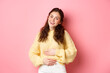 © Mix and Match Studio - Young smiling woman touching her stomach with relieved, happy face, feeling good after eating yoghurt or medicine from painful cramps, standing against pink background