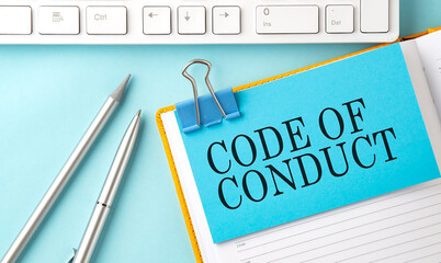 CODE OF CONDUCT text on sticker on the blue background with pen and keyboard