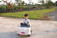Cute Asian Kid Driving Electric Toy Car Auto Home Backyard On Nature In Summer. Outdoor Toys, Little 5 Years Old Kindergarten Schoolboy In Battery-powered Ride-on Car Vehicle