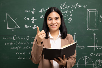 Wall Mural - Young asian teacher woman teaching holding book and video conference with student looking camera. Female teacher training the mathematics in classroom blackboard from online course.