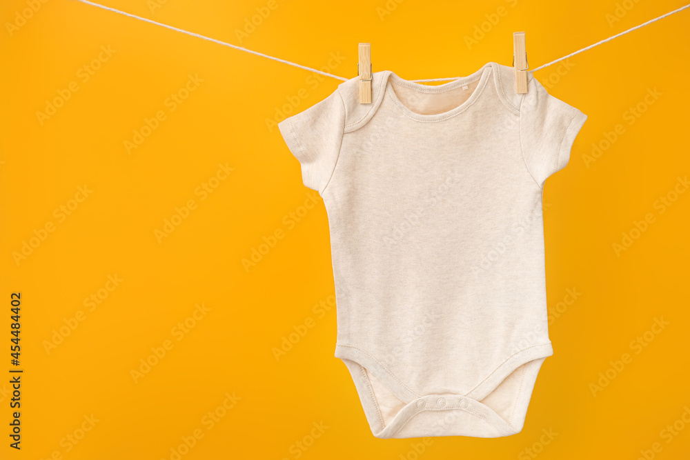 Baby clothes hanging on rope against color background