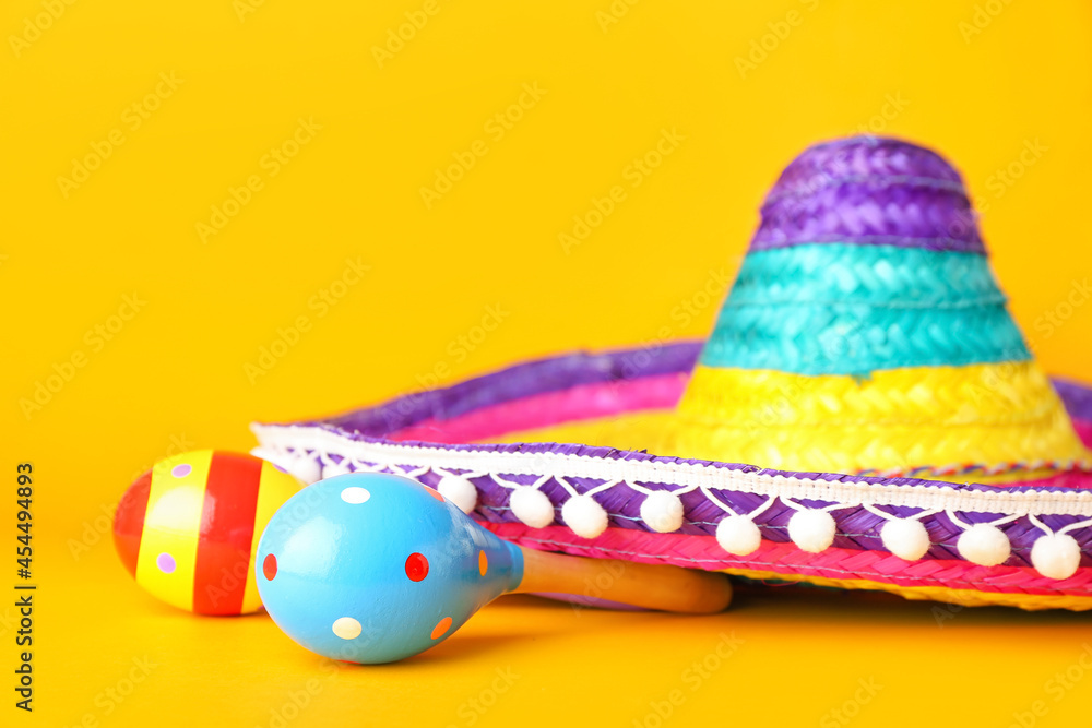 Mexican maracas and sombrero on color background