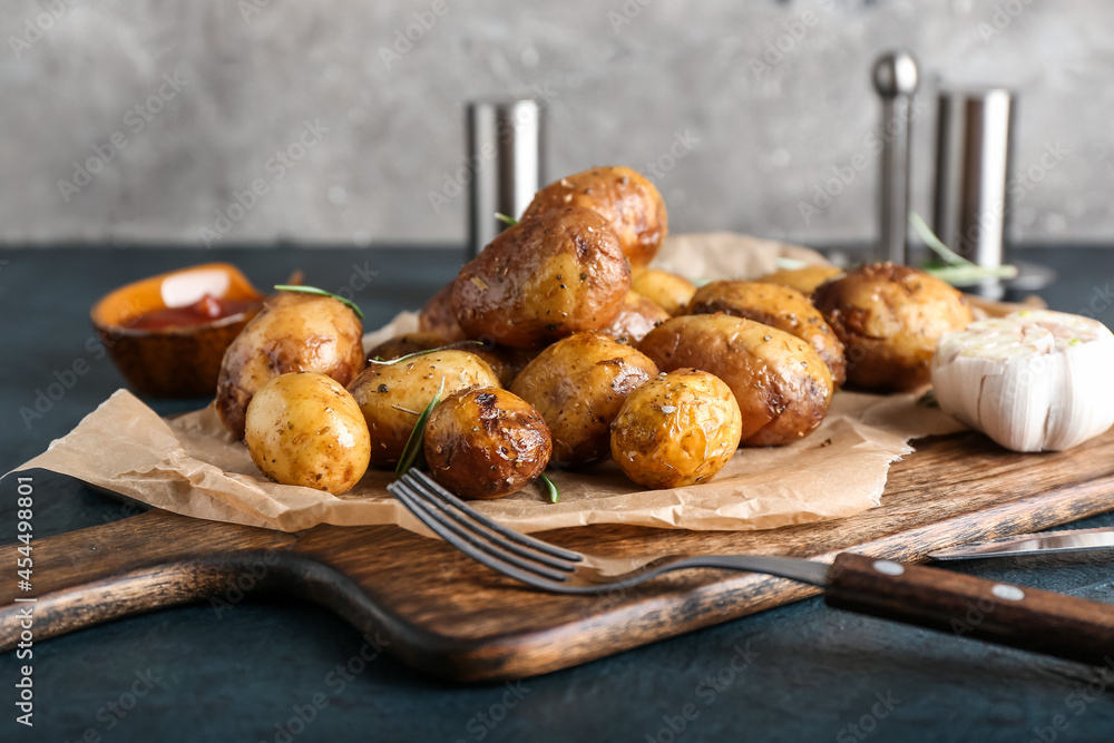 Board with baked potatoes and rosemary on dark background