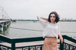 © Natalia Rzhevskaia - A happy girl on the river bank, standing on the bridge, smiling, a girl walks on the bridge by the river. Freedom. The wind is blowing the girl's hair.