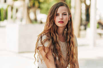 Poster - Portarit of a beautiful Caucasian young woman resting on the street. A beautiful female has a joyful expression while sitting outdoors. Mental health concept.