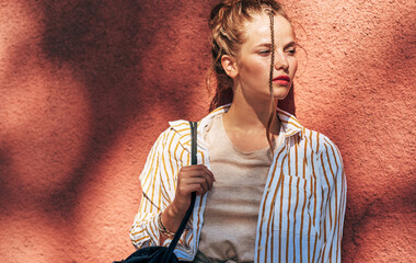 Poster - Outdoor portrait of young woman looking at one side on a sunny day against a red wall. Young female student posing in the city street.