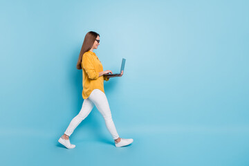 Wall Mural - Full length profile side photo of attractive woman hold laptop walk empty space isolated on blue color background