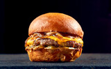 Fototapeta  - Juicy burger with beef, cheese, caramelized onions and tomato, sauce on a dark background.